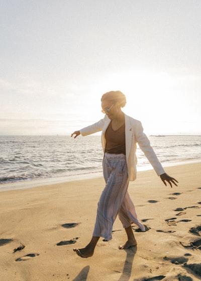 穿着白色长袖衬衫和灰色裤子的女人白天在沙滩上散步